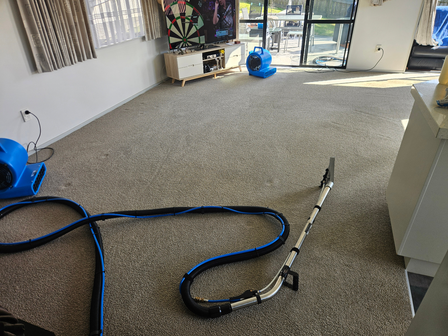 Carpet cleaning in progress – blue hoses and blower fans in open-plan living room with darts board