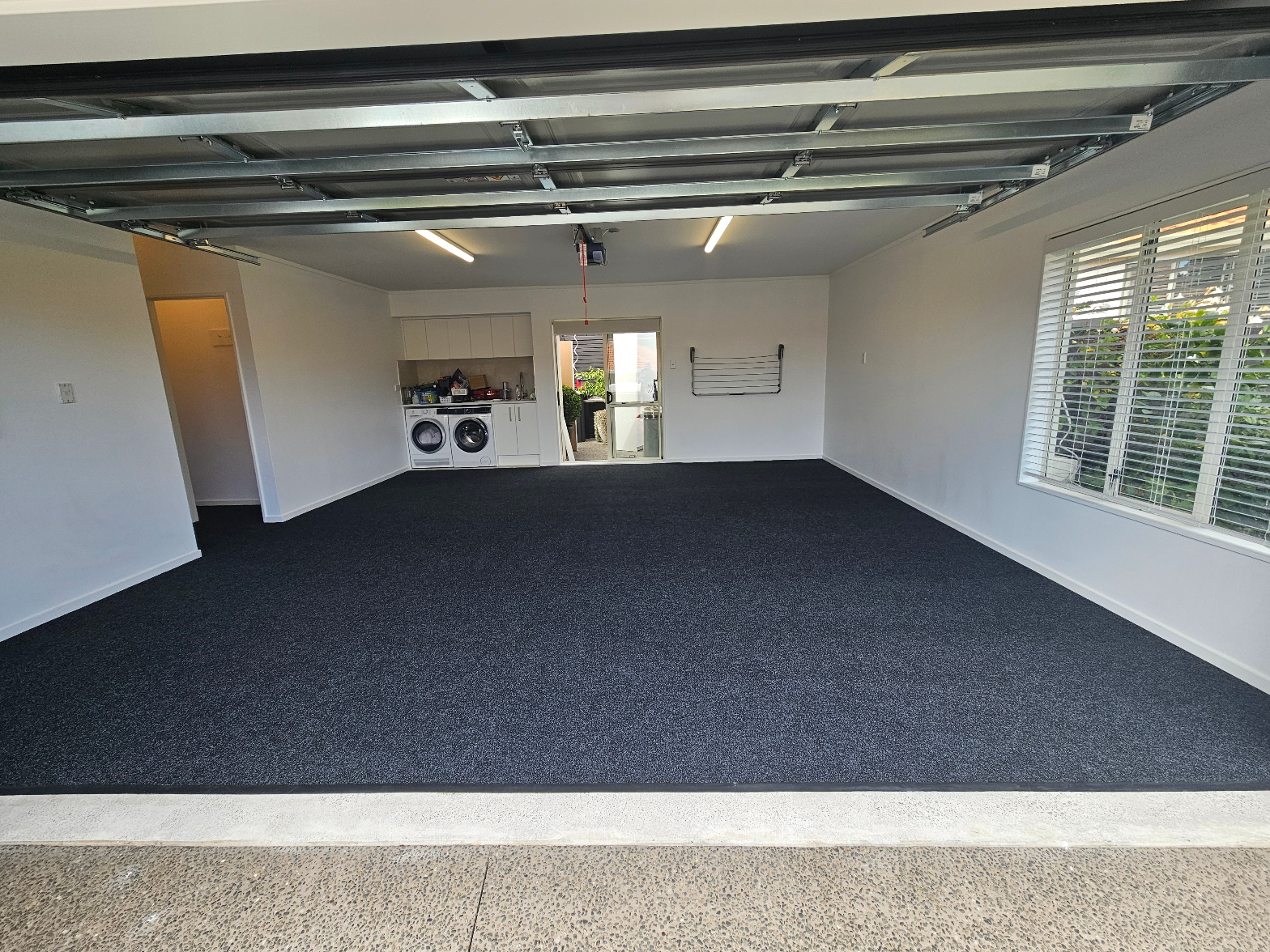 Dark charcoal carpet fully installed in a modern double garage with laundry area and roller door open